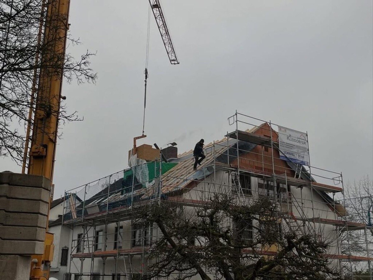 Bauarbeiter auf einem Hausdach unter einem Kran bei der Aufstockung