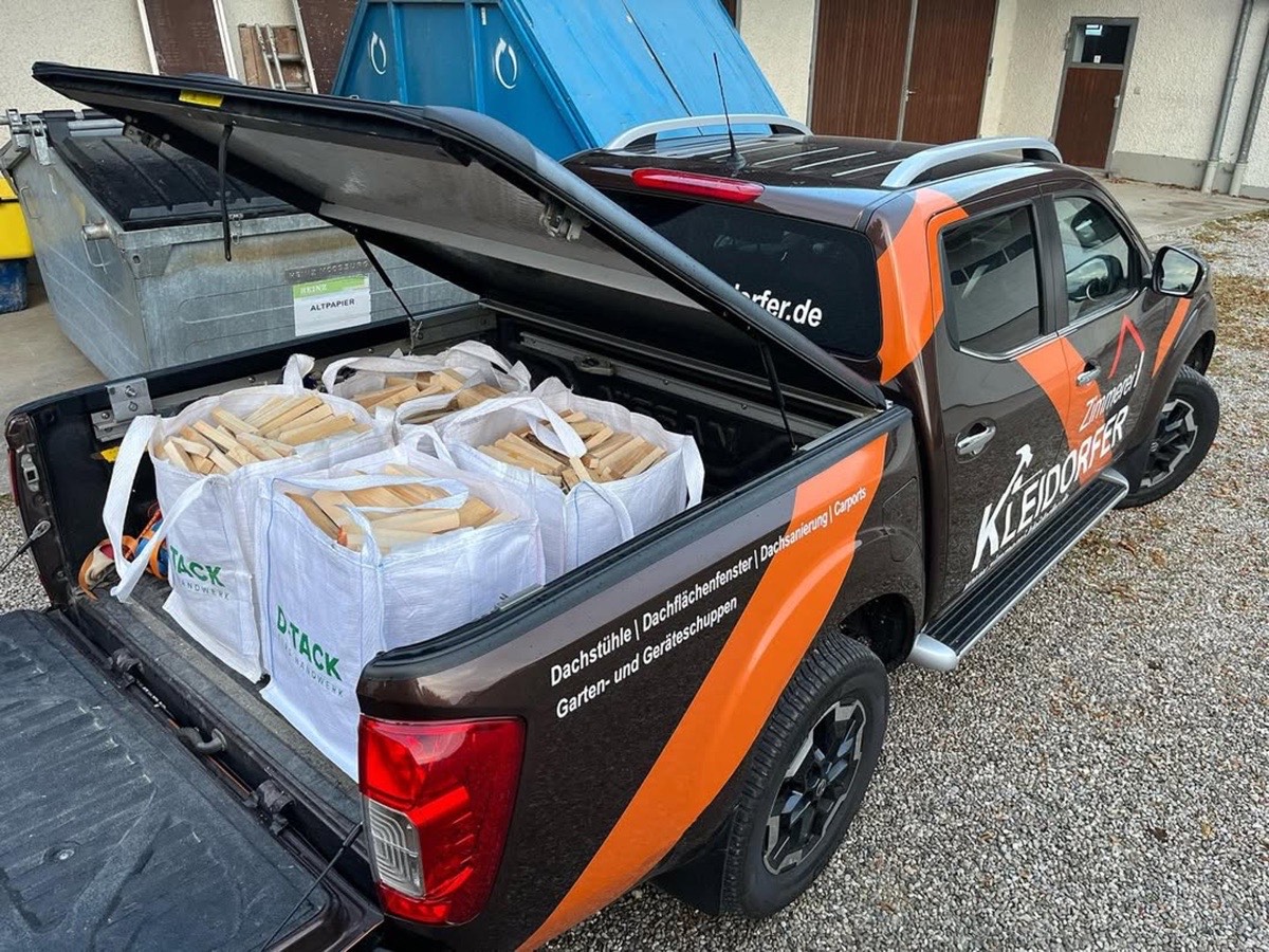 Brauner Pickup-Truck mit offener Ladefläche, gefüllt mit weißen Säcken voller Holzscheite.