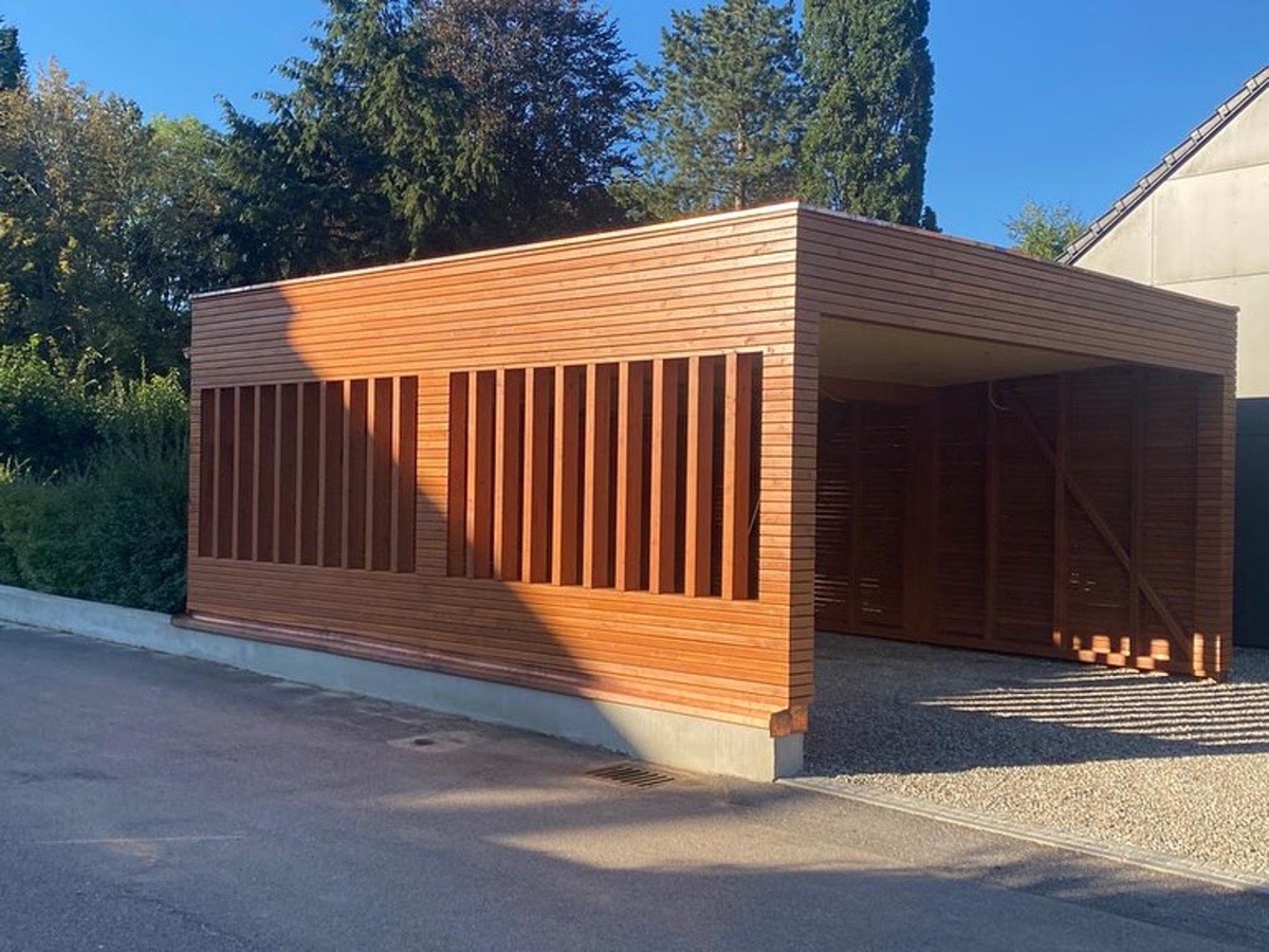 Modernes Carport aus Holzlamellen neben einer Asphaltstraße unter blauem Himmel.