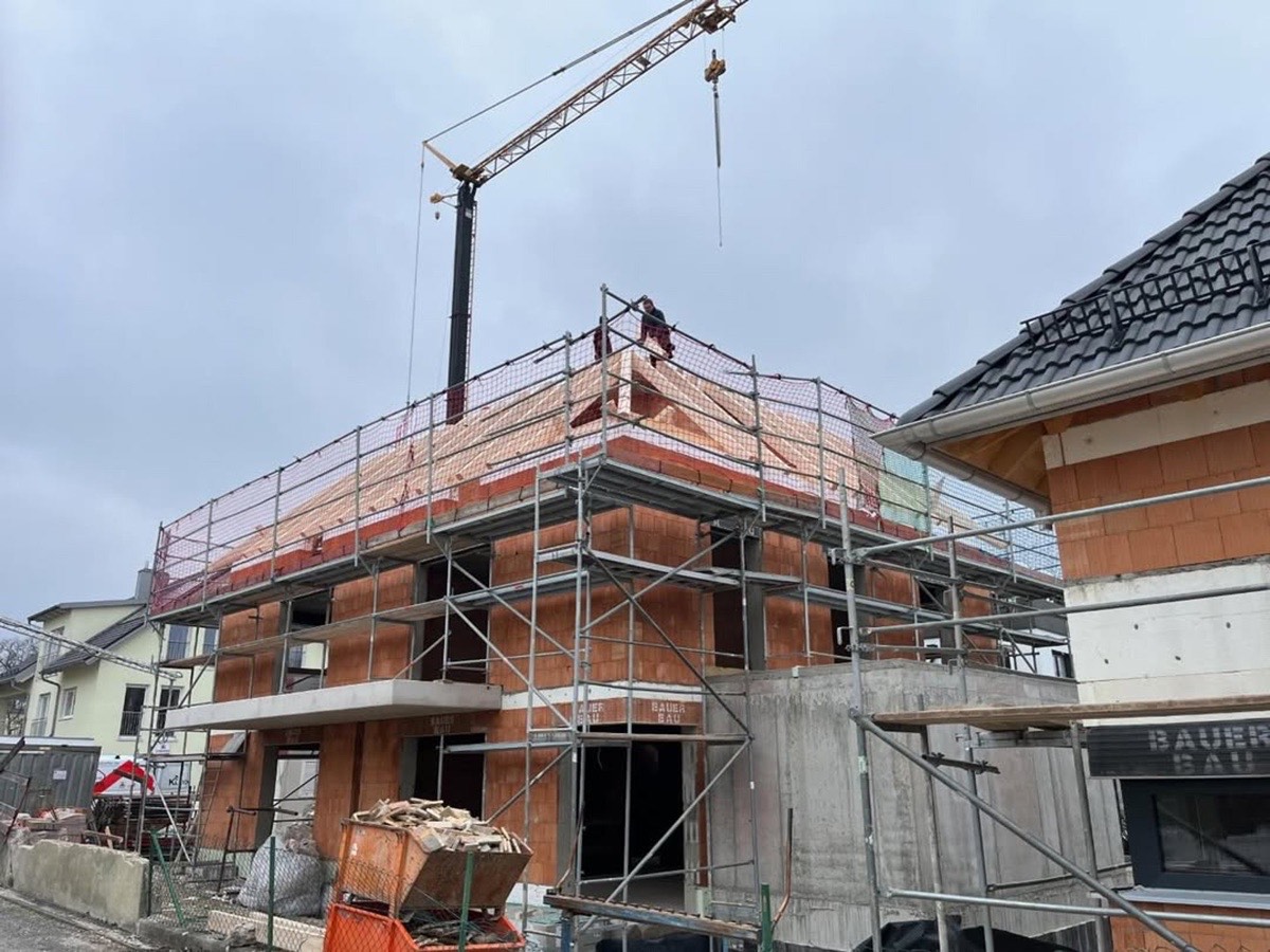 Baustelle eines Hauses mit Gerüst, Baugerüst, Kran und teilweise fertigem Dach.