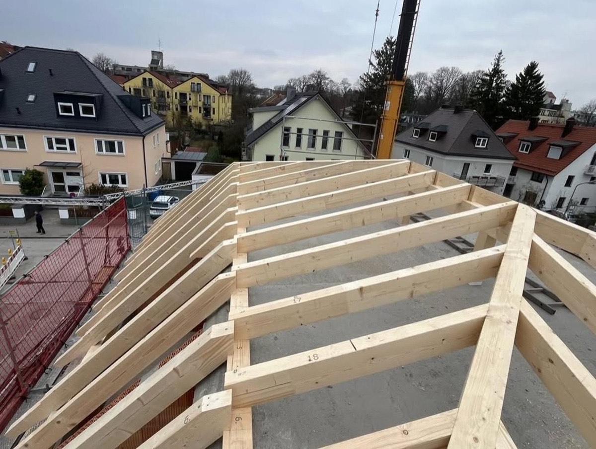 Neuer Holzdachstuhl eines Hauses im Bau, mit Gebäuden und einem Kran im Hintergrund.