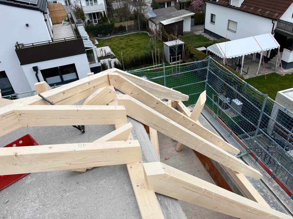 Dachstuhl aus hellem Holz auf einem Neubau, umgeben von Häusern und Gärten.