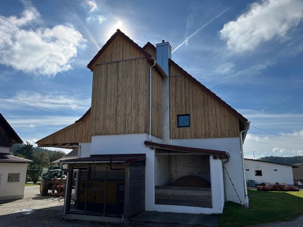 Ein rustikales, weiß getünchtes Scheunengebäude mit Holzdach und Verkleidung unter strahlendem Sonnenschein.