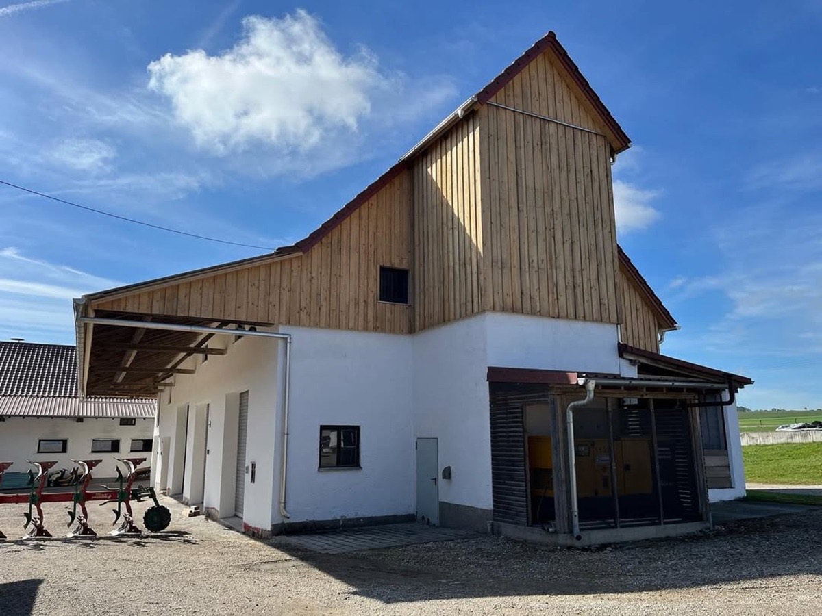 Großer weißer Bauernhof mit Holzdach und blauem Himmel.