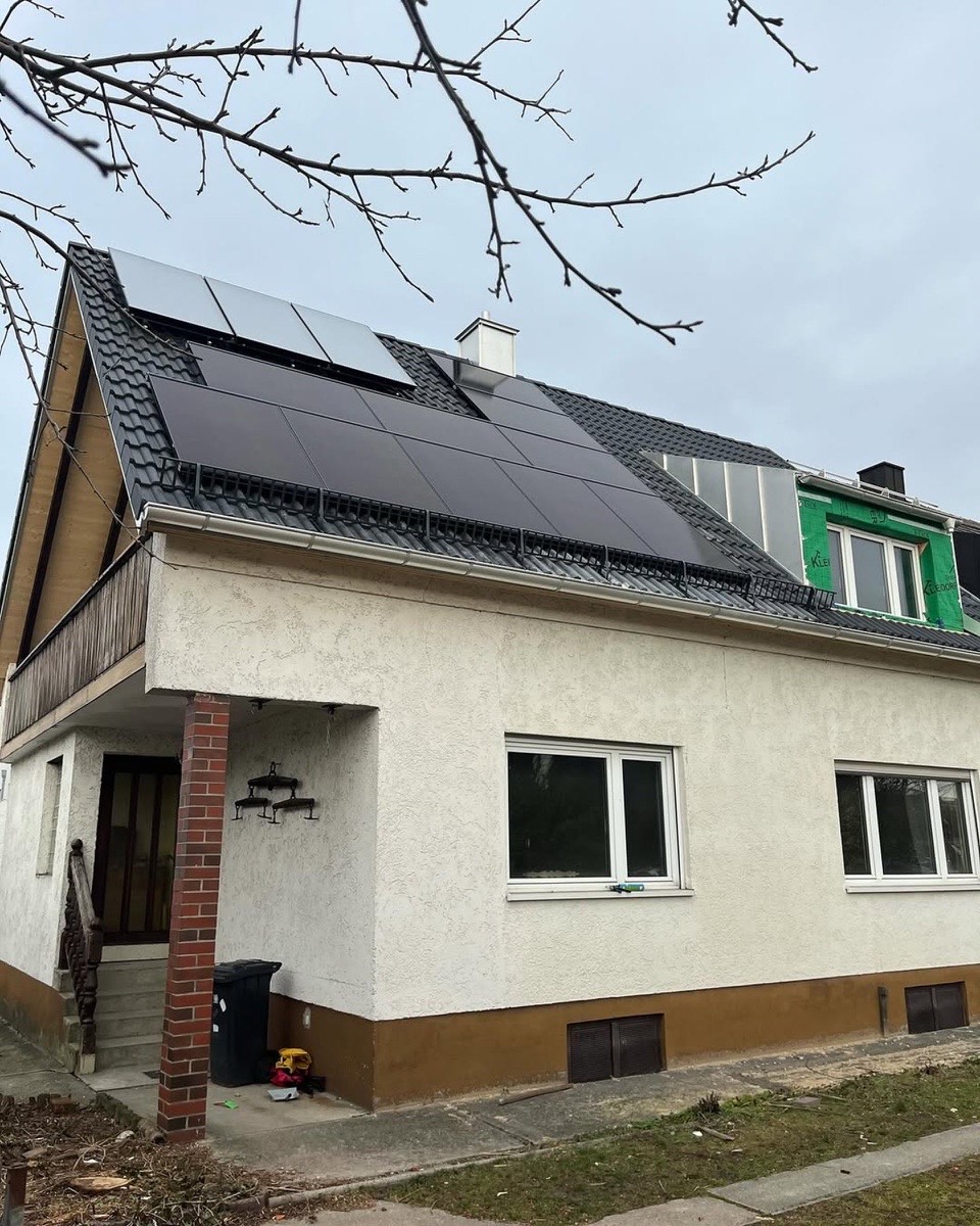 Haus mit schwarzem Dach und Solarpaneelen, teils mit Gerüst und grüner Isolierung.