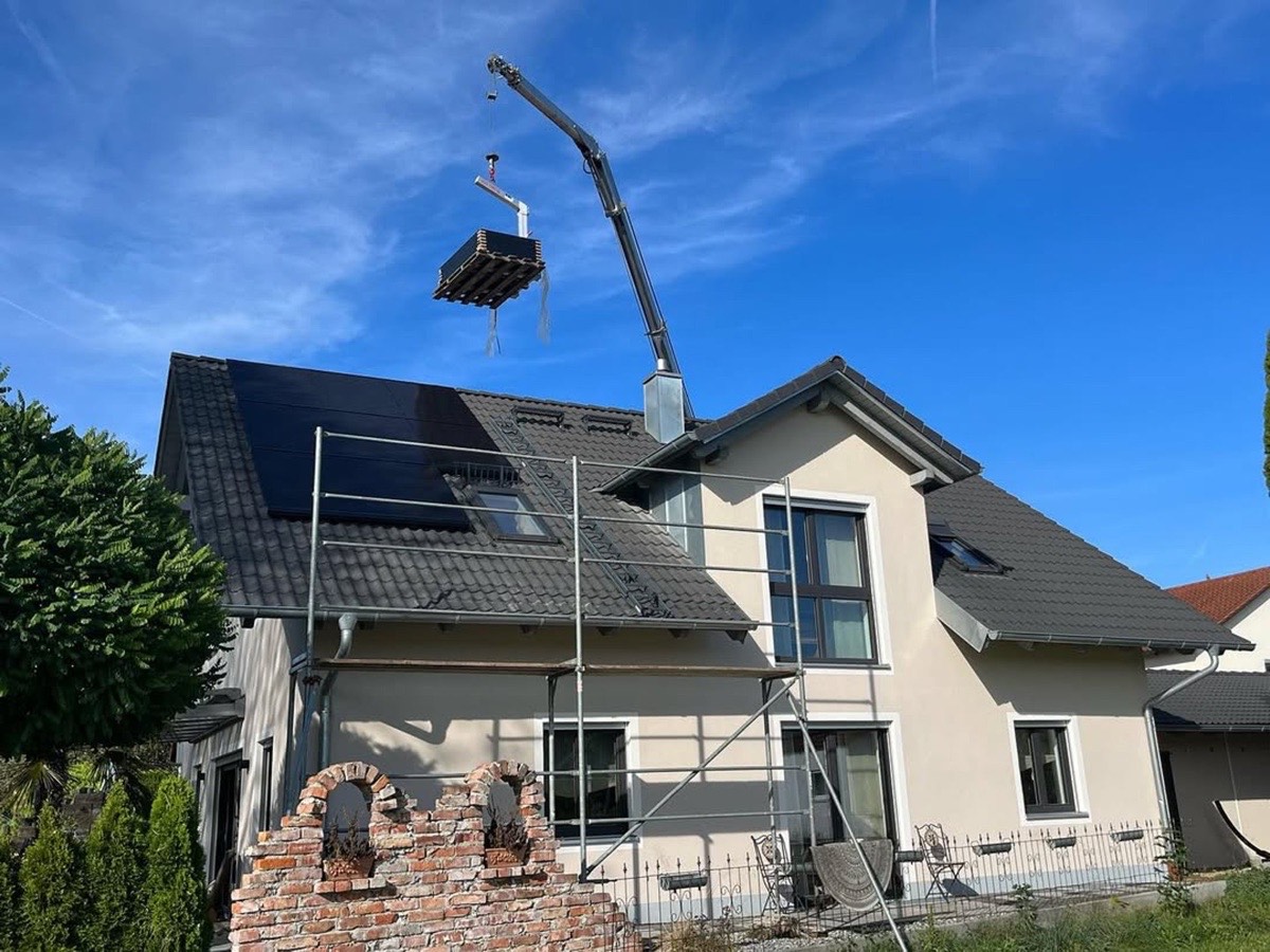 Ein Kran hebt eine rechteckige Plattform über ein Haus