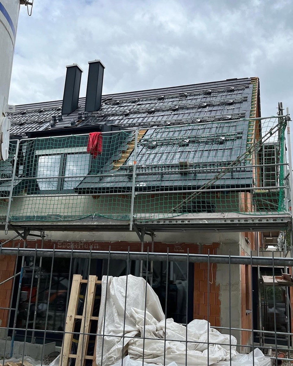 Eine Baustelle mit einem teilweise gedeckten Dach, auf dem zwei schwarze Schornsteine und ein rotes Tuch zu sehen sind.