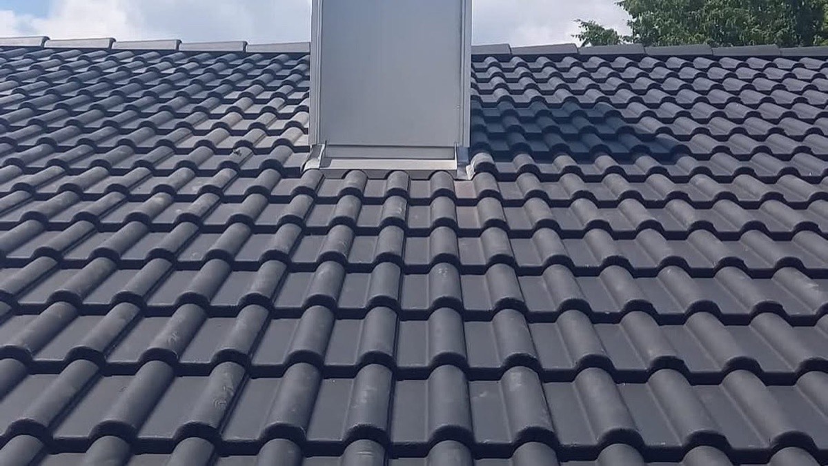 Dunkelgraues Ziegeldach mit einem Dachfenster und einem weißen Schornstein.
